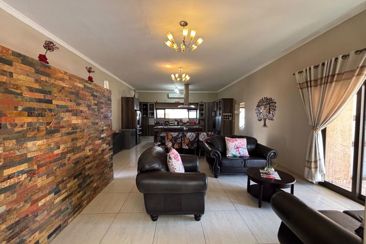 Spacious open-plan living and kitchen area featuring a decorative stone feature wall, neutral tiled flooring, and modern kitchen cabinetry with an island.