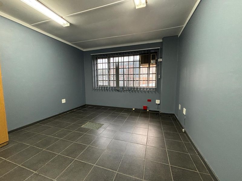 An empty office space featuring dark tiled flooring, security bars on the window, and a built-in air conditioning unit.