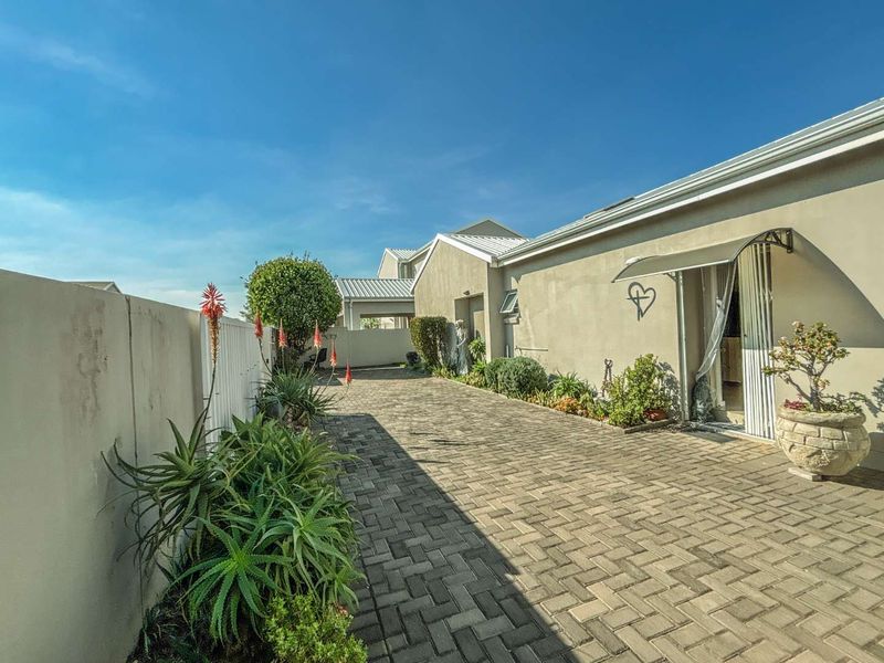 A paved side walkway or courtyard area featuring a boundary wall, established garden beds, and access to the main dwelling via a sliding door.