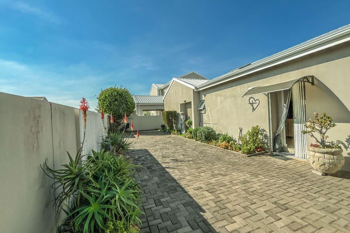 A paved side walkway or courtyard area featuring a boundary wall, established garden beds, and access to the main dwelling via a sliding door.