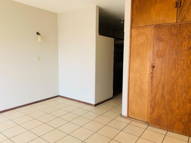 An empty bedroom featuring ceramic floor tiles, a built-in wooden wardrobe, and a wall-mounted light fixture, offering a blank canvas for renovation.