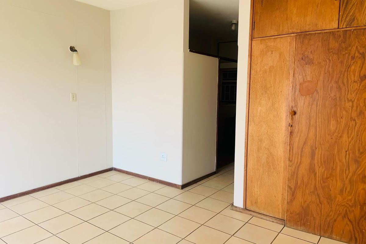 An empty bedroom featuring ceramic floor tiles, a built-in wooden wardrobe, and a wall-mounted light fixture, offering a blank canvas for renovation.