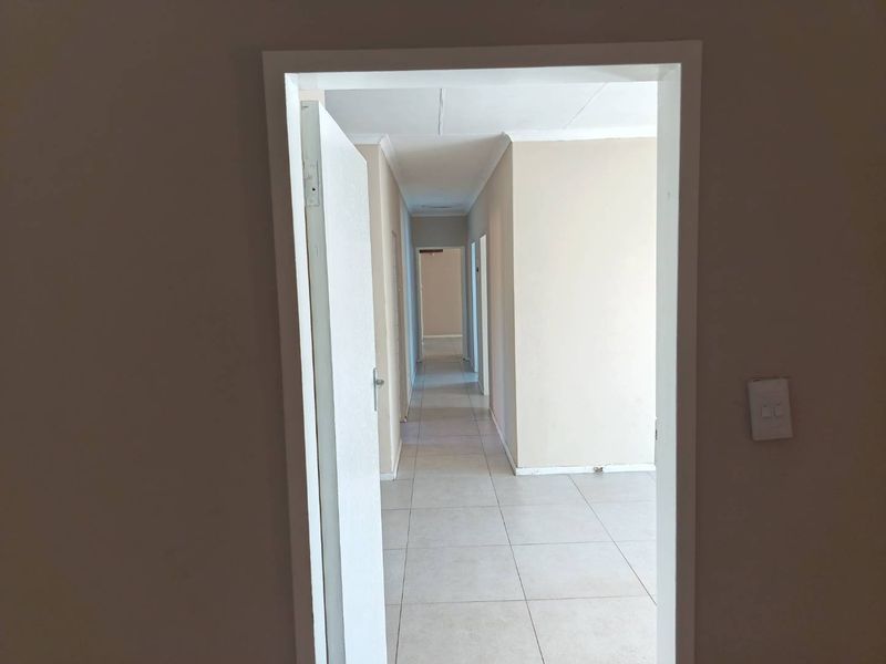 A long, empty hallway featuring neutral wall paint and light-colored floor tiles, providing access to multiple rooms within the home.