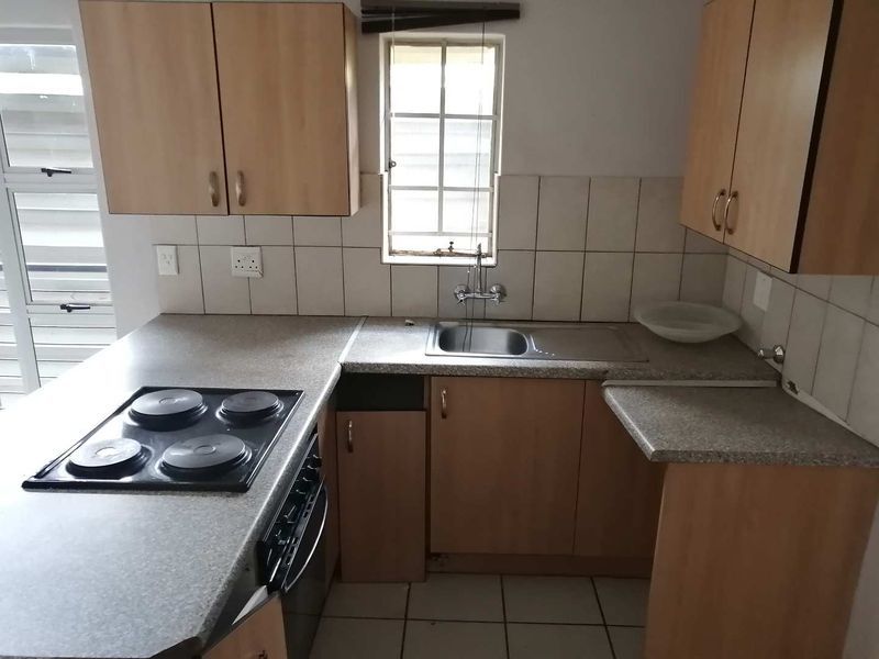 A compact kitchen featuring laminate countertops, built-in cabinetry, an electric hob, and a stainless steel sink, currently requiring minor repairs and cosmetic updates.