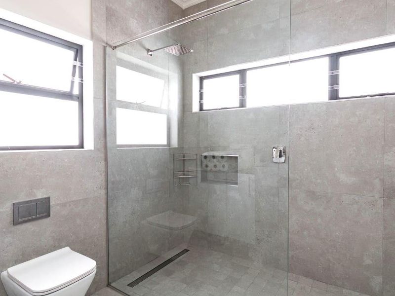 Modern bathroom featuring a spacious walk-in shower with a glass screen, rain shower head, recessed niche, and a sleek wall-mounted toilet with concealed cistern.