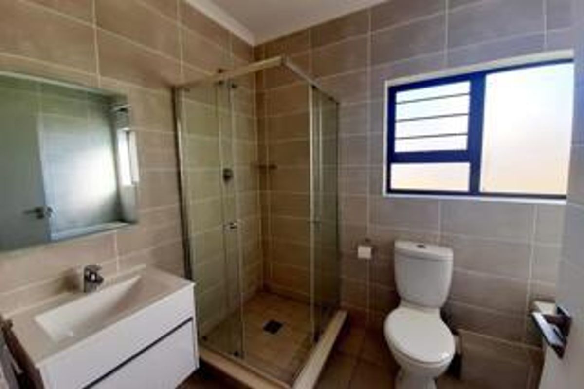 A modern bathroom featuring a glass-enclosed shower, a wall-mounted vanity with basin, a toilet, and neutral floor-to-ceiling wall tiles.