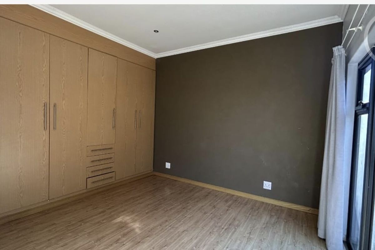 A spacious bedroom featuring extensive built-in wooden cupboards, laminate flooring, and a sliding door providing natural light.