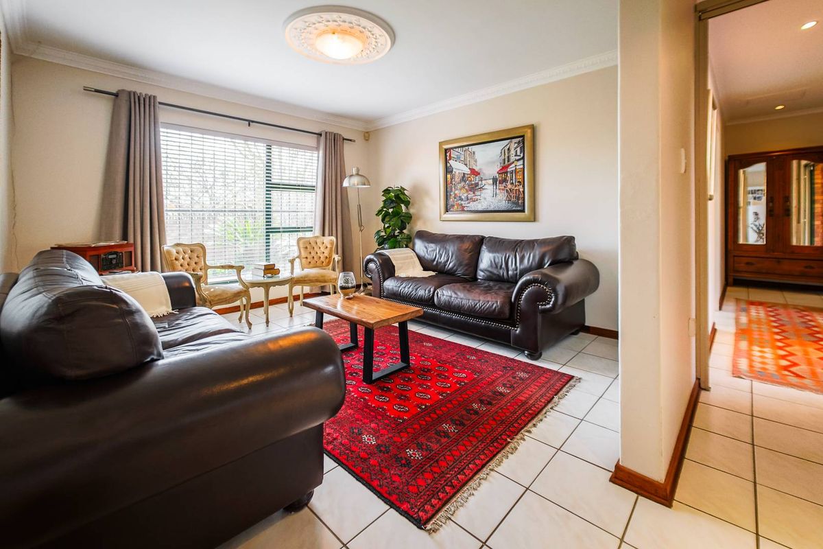 A comfortable living room featuring tiled flooring, decorative ceiling rose, and coving, with a large window providing natural light.