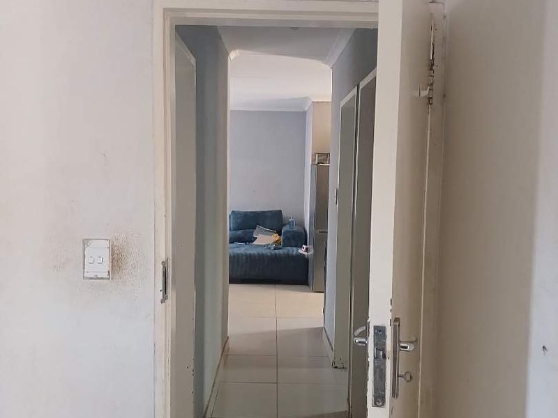 A view through a doorway into a tiled hallway leading to an adjacent living space, showing signs of wear on the walls and door frames.