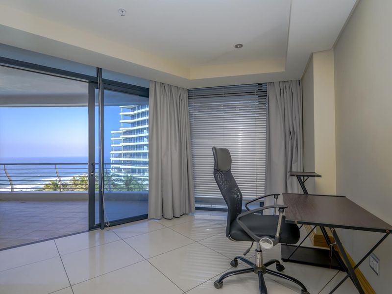 A bright office space featuring large sliding glass doors that open onto a balcony with scenic ocean and coastal views.