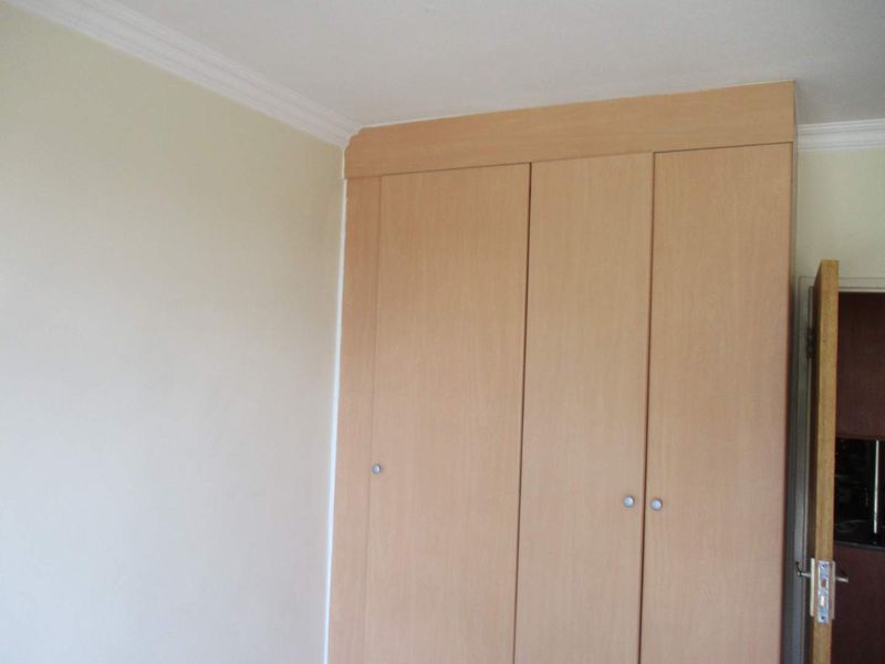 A bedroom featuring a light wood-finish built-in wardrobe with integrated cornice detailing.