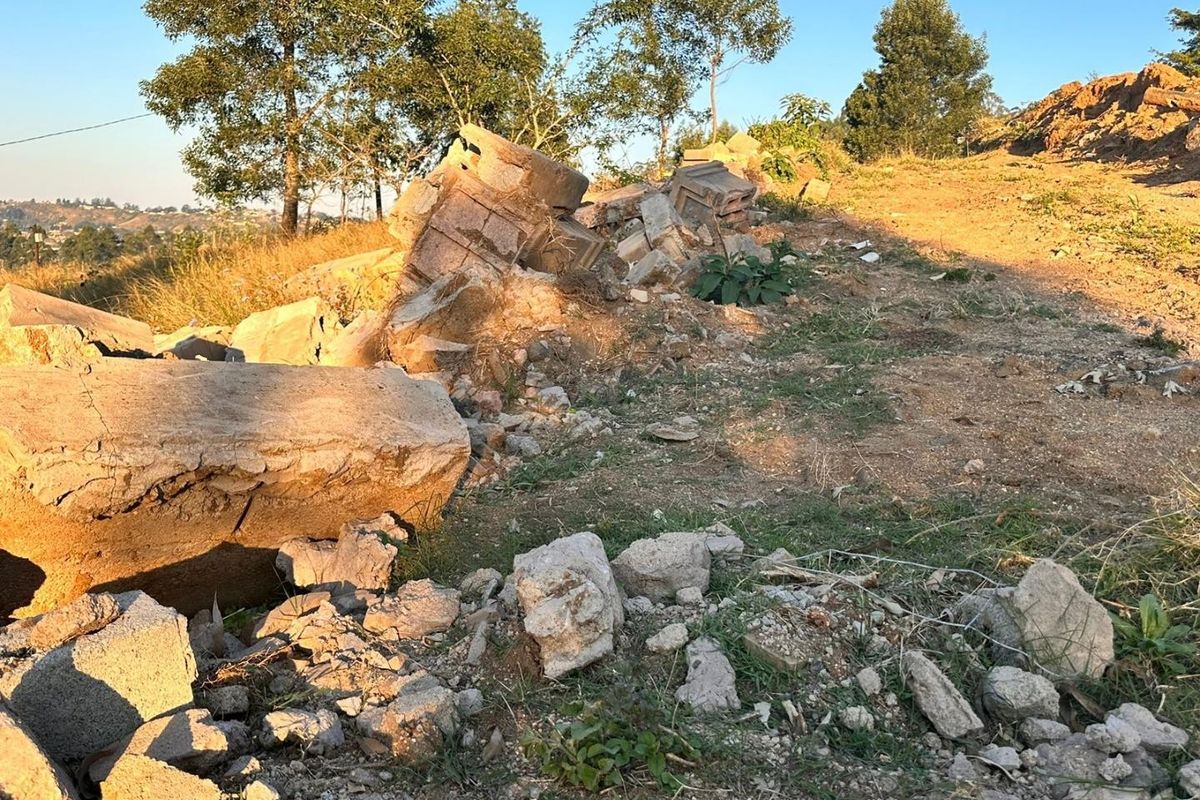A view of a sloped residential plot featuring scattered construction debris and rubble, requiring site clearing for future development.