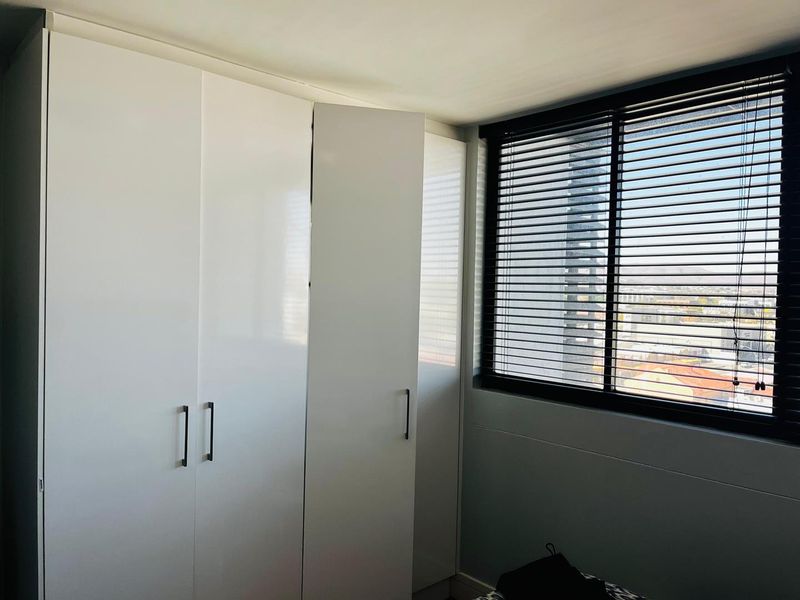 A bright bedroom featuring modern white built-in cupboards and dark venetian blinds, offering a clean and functional storage solution.