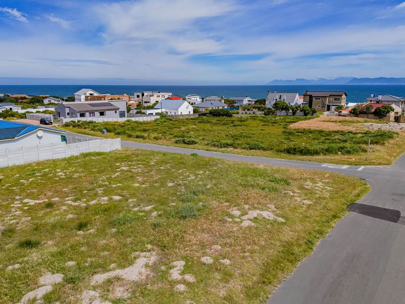 An aerial view of a vacant residential plot situated in a coastal neighborhood with established road access and ocean views.