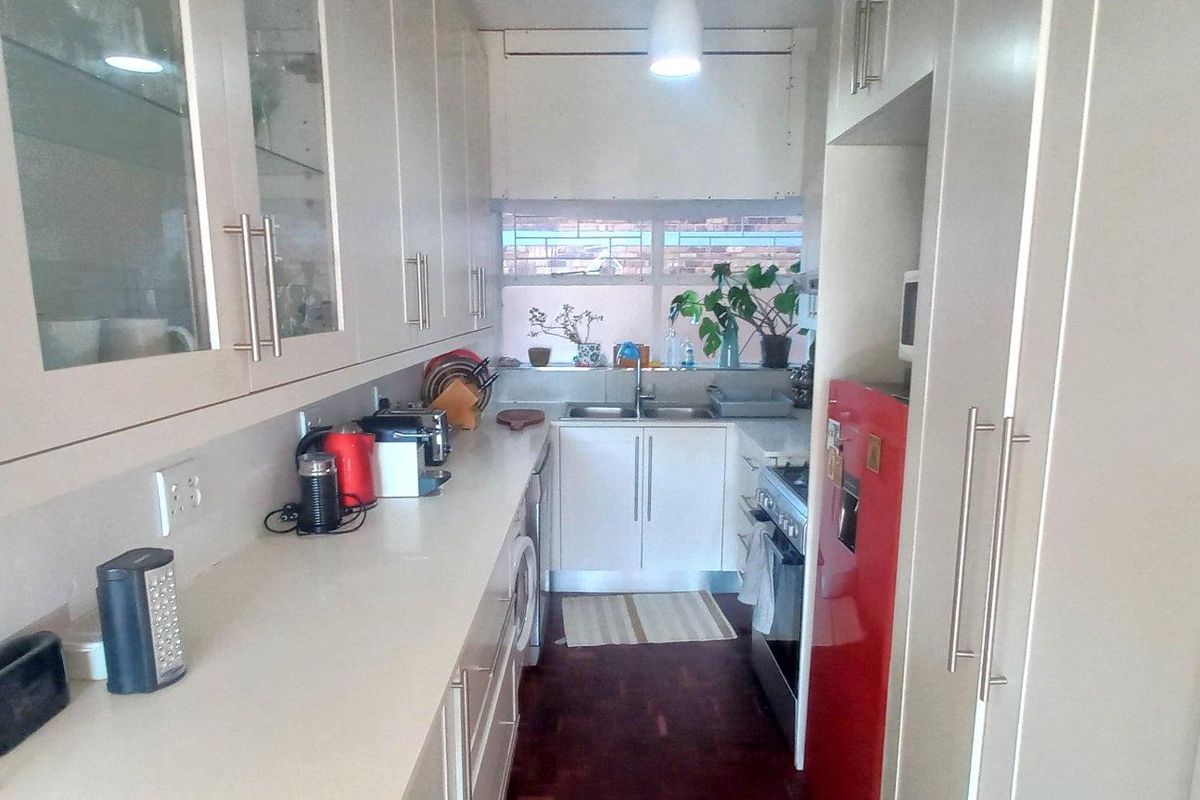 A galley-style kitchen featuring white cabinetry, ample counter space, a double sink, and integrated appliance space.