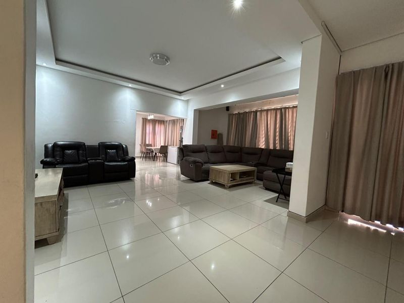 Spacious open-plan living area featuring neutral porcelain floor tiles, recessed ceiling details, and integrated downlighting, creating a bright and versatile living space.