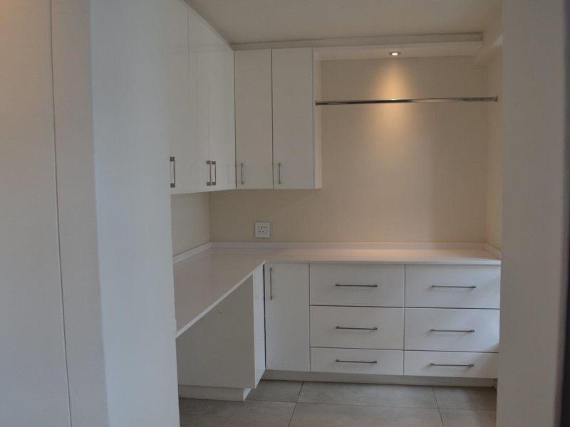 A clean and functional laundry area featuring ample white built-in cabinetry, laminate countertops, and integrated lighting.