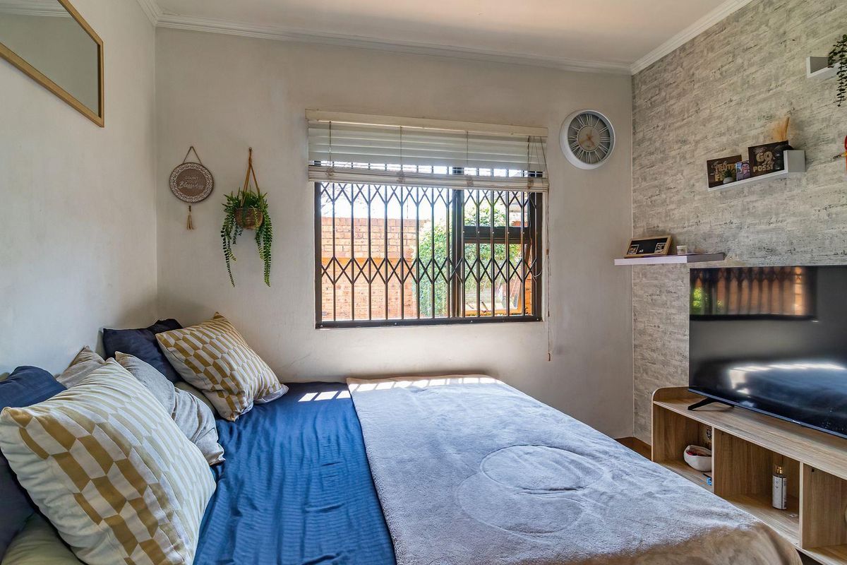 A cozy bedroom featuring a textured accent wall, security gate on the window, and venetian blinds for privacy.
