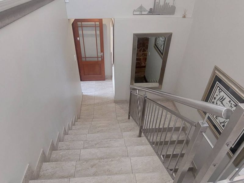 A bright hallway featuring a tiled staircase with a modern stainless steel balustrade leading to a timber entrance door.