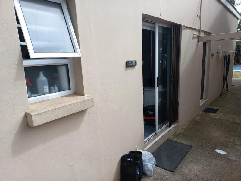 Rear exterior view of the apartment featuring a sliding glass door entrance and a top-hung window with concrete pathway access.