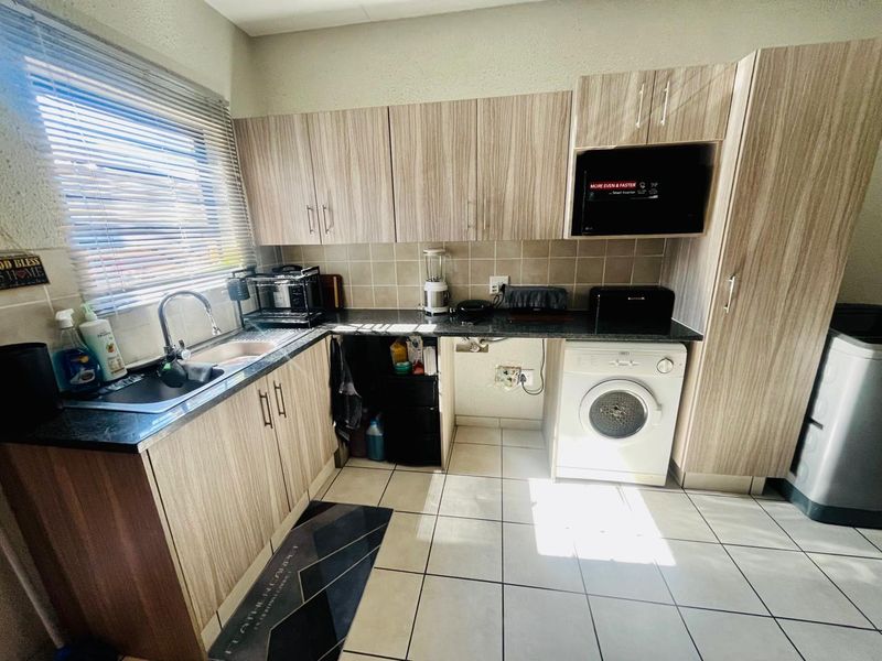 A functional kitchen featuring wood-look laminate cabinetry, granite countertops, a tiled backsplash, and dedicated plumbing for a washing machine.
