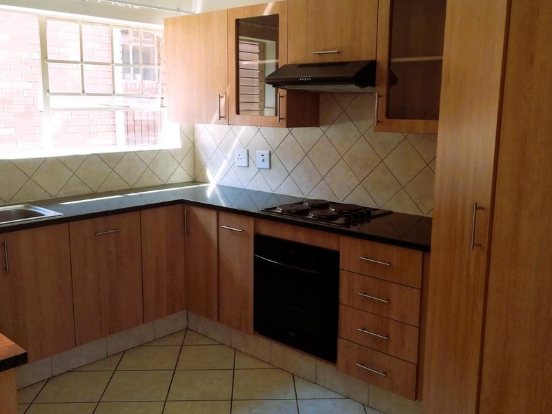 A functional kitchen featuring wood-look laminate cabinetry, dark granite countertops, built-in oven, electric hob, extractor fan, and tiled flooring.