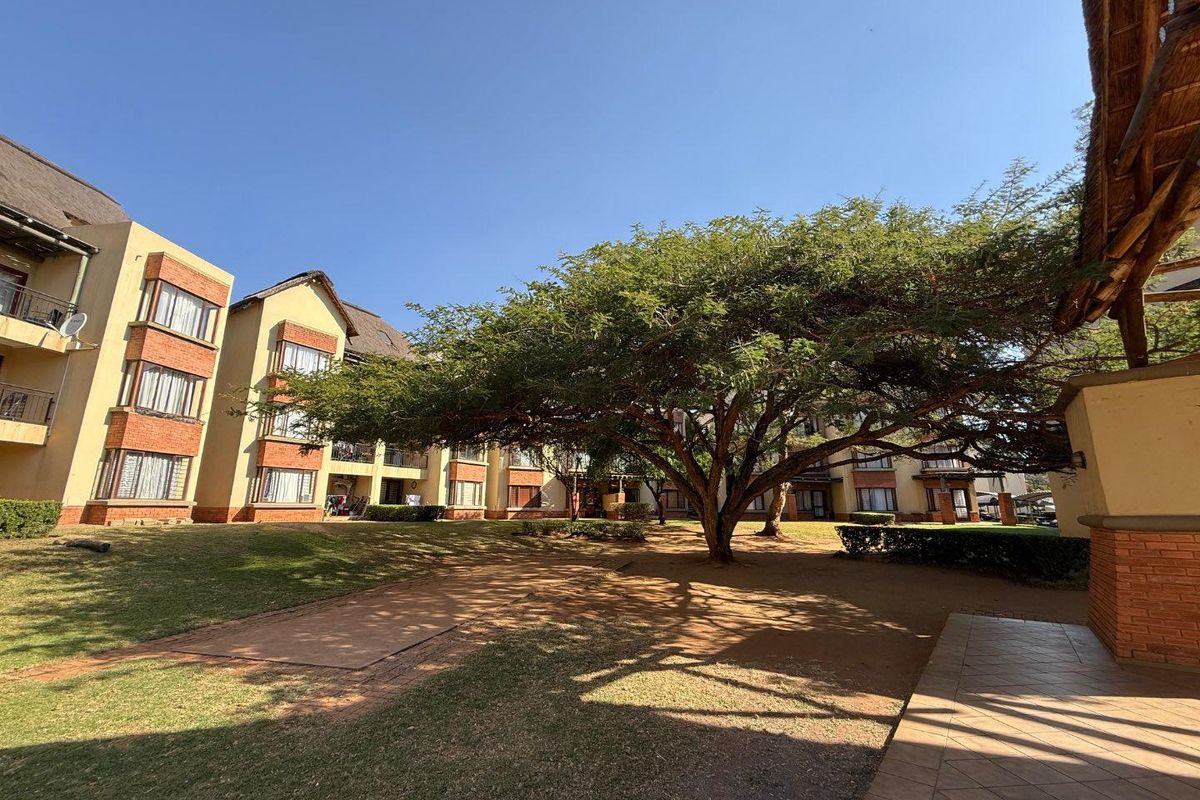 A view of the apartment complex exterior featuring landscaped gardens, mature trees, and traditional brick and thatched roof architecture.