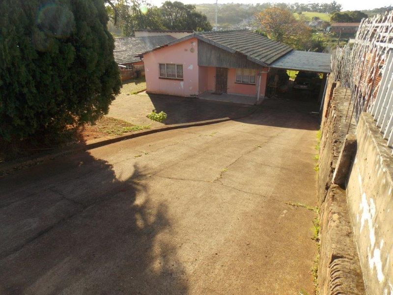Front view of a single-story house featuring a concrete driveway, attached carport, and perimeter boundary wall with security spikes.