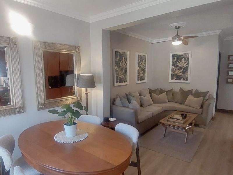 An open-plan living and dining area featuring laminate flooring, crown molding, and a ceiling fan, creating a cohesive and functional living space.