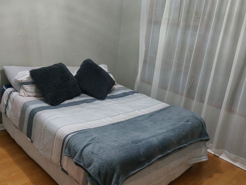 A compact bedroom featuring laminate flooring and a window fitted with security bars.