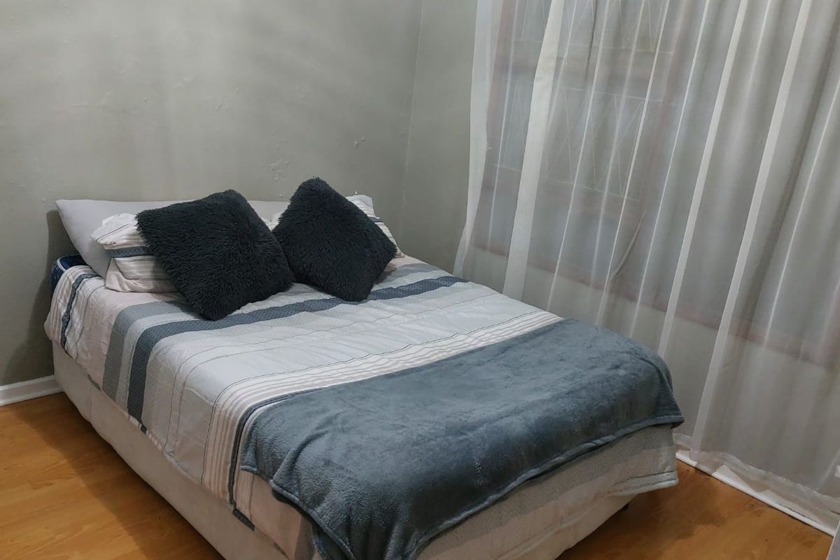 A compact bedroom featuring laminate flooring and a window fitted with security bars.