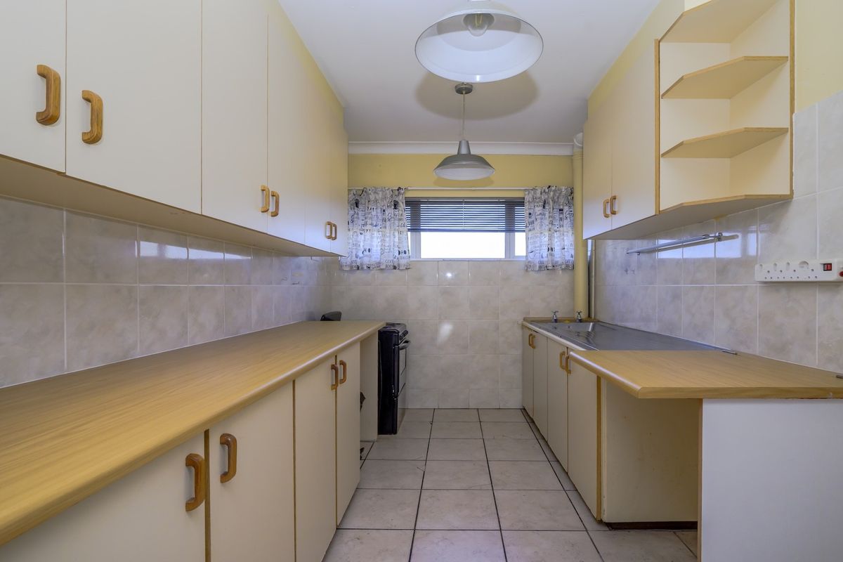 A functional, galley-style kitchen featuring ample built-in cabinetry, laminate countertops, tiled splashbacks, and a stainless steel sink, offering a blank canvas for renovation.