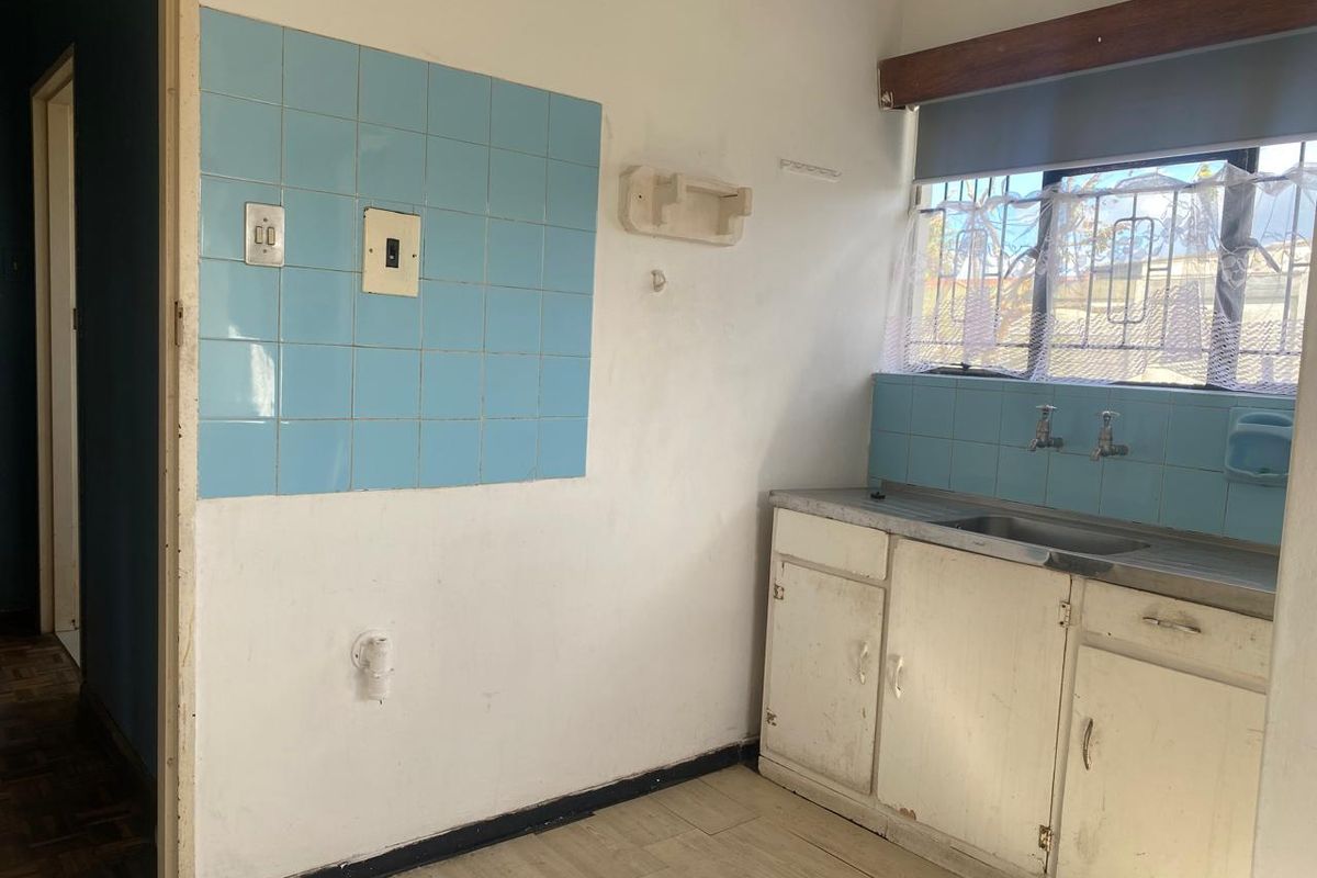 A compact kitchen area featuring a single sink, dated cabinetry, and blue tiled splashbacks, requiring modernization to improve functionality and aesthetic appeal.