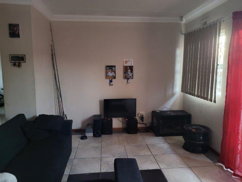 A living room area featuring tiled flooring, cornicing, and vertical blinds, providing a functional space for relaxation.