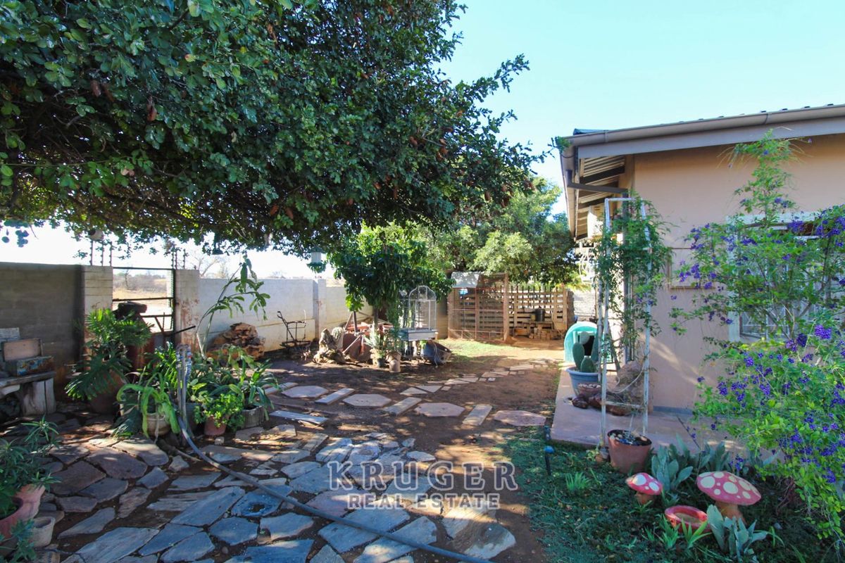 A rear garden area featuring stone paving, mature trees, and a boundary wall, providing a private outdoor space adjacent to the house.