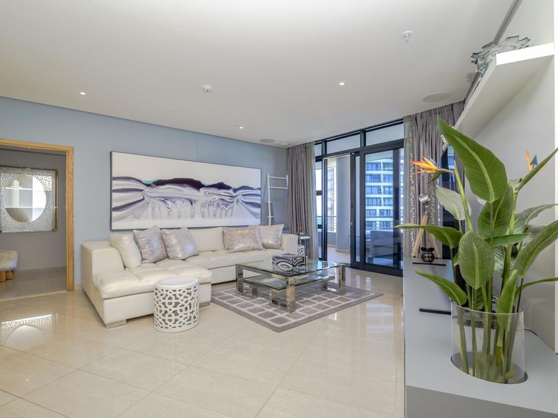 A bright and modern living room featuring tiled flooring, recessed lighting, and large sliding glass doors leading to an outdoor balcony area.