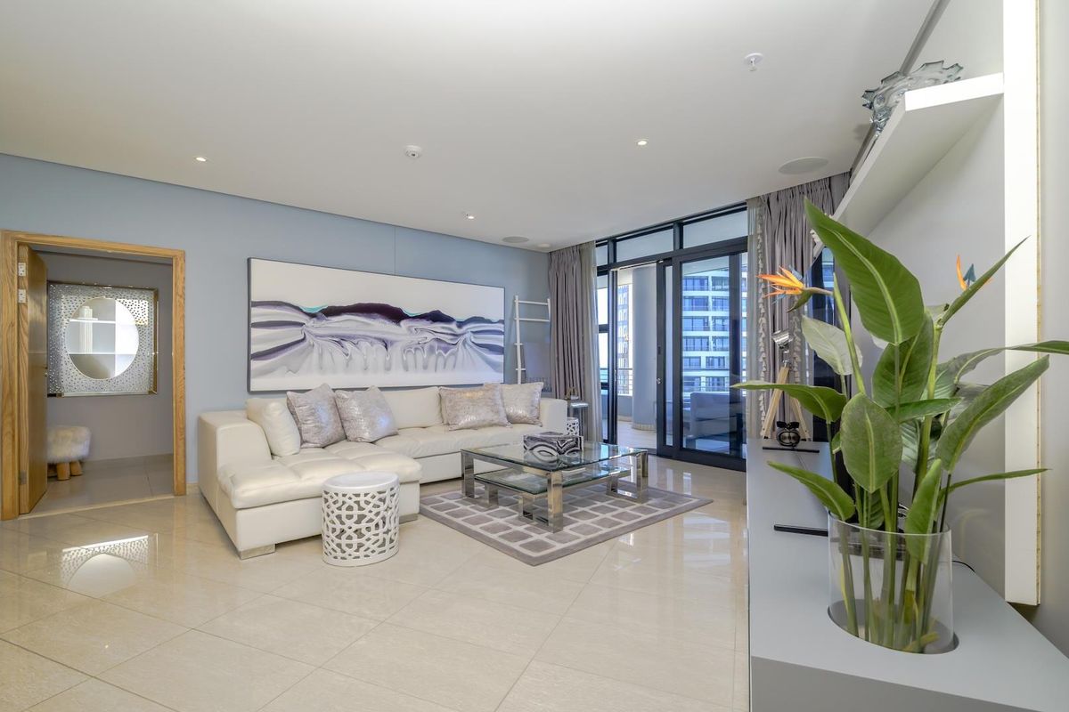 A bright and modern living room featuring tiled flooring, recessed lighting, and large sliding glass doors leading to an outdoor balcony area.