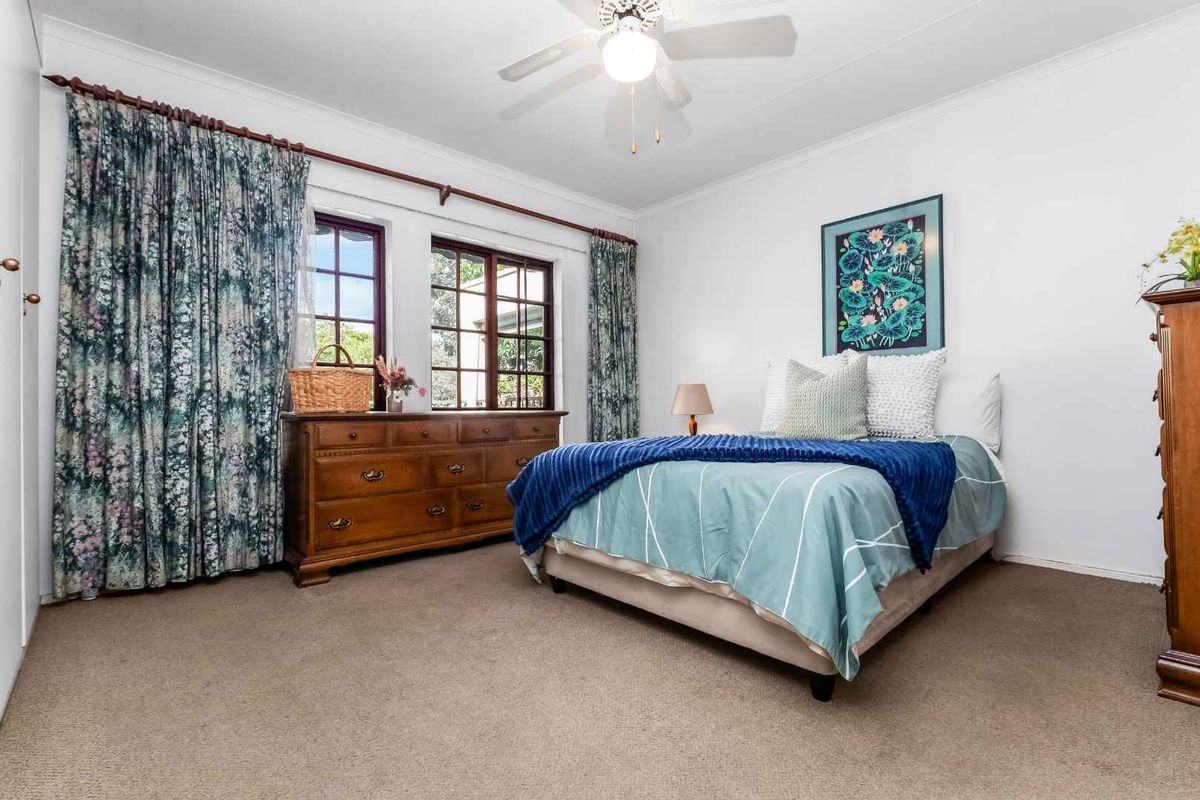 A well-lit bedroom featuring neutral carpeting, a ceiling fan, and large windows with classic timber frames.