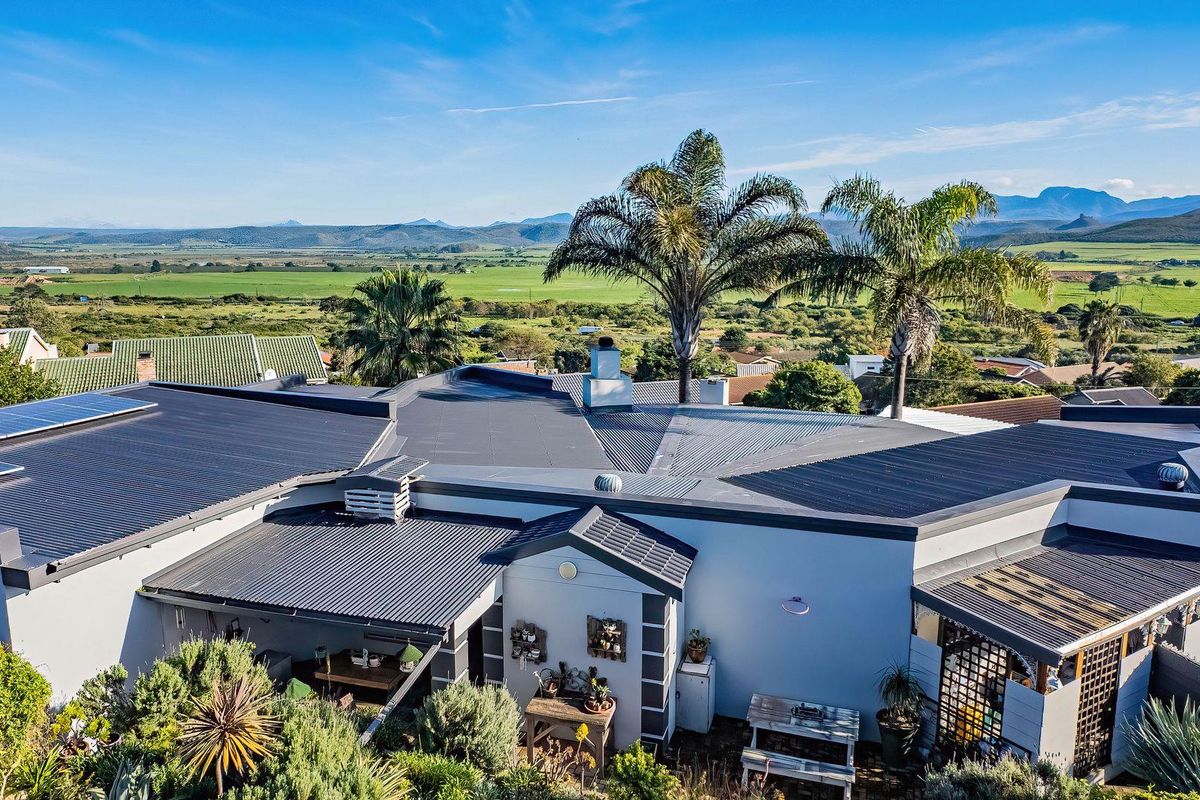 Aerial view of the property featuring a modern corrugated metal roof, integrated solar panels, and a scenic rural landscape backdrop.