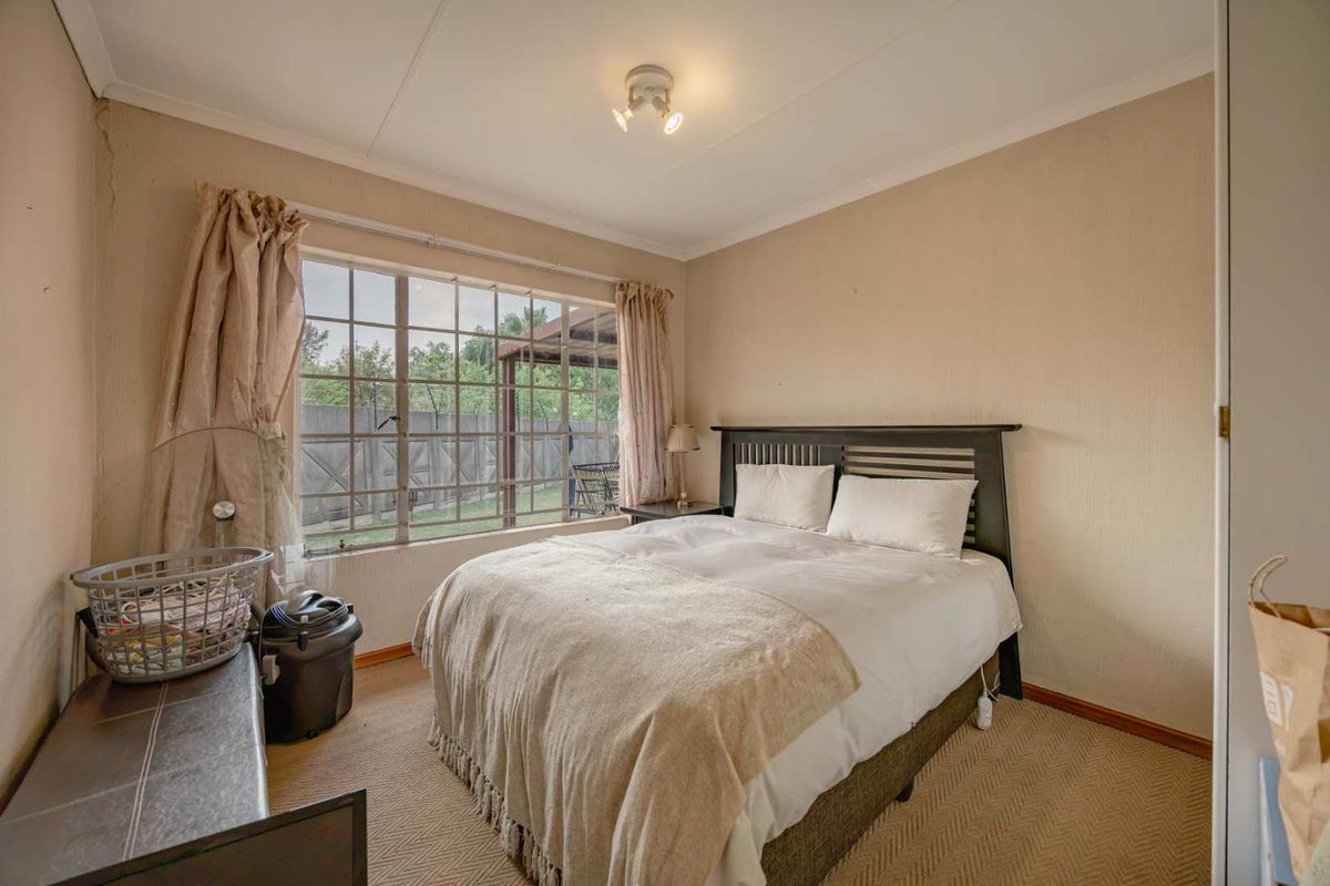 A bedroom featuring a large window with garden views, carpeted flooring, and a built-in cupboard, offering a functional space with potential for cosmetic updates.