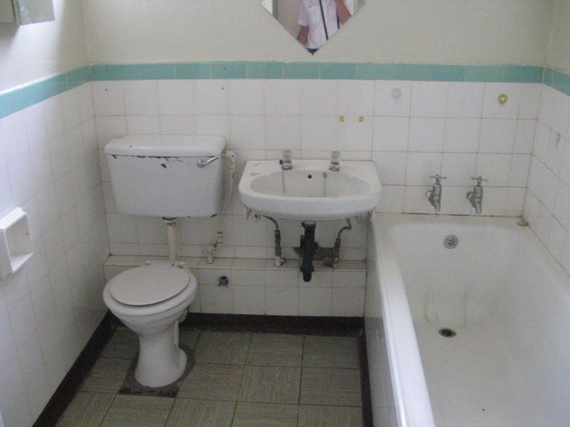 A dated bathroom featuring original ceramic tiling, a standard bathtub, pedestal basin, and toilet, requiring modernization of fixtures and finishes.