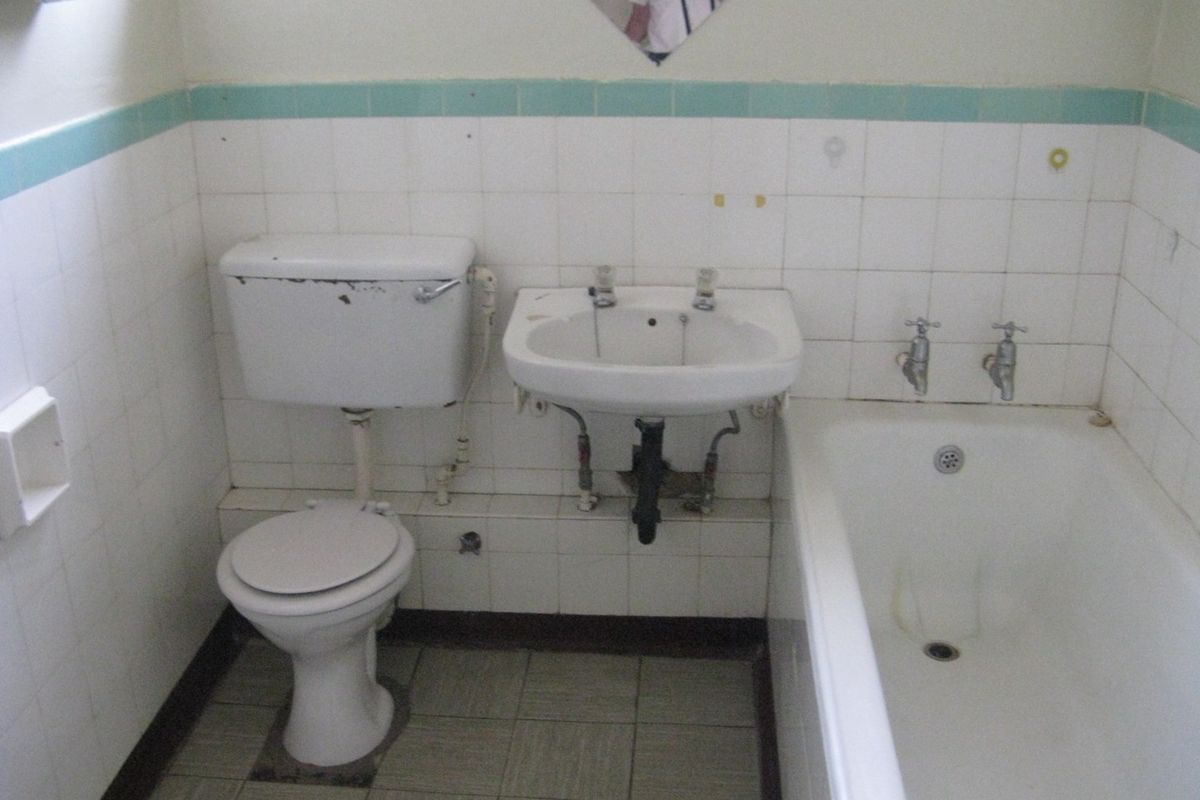 A dated bathroom featuring original ceramic tiling, a standard bathtub, pedestal basin, and toilet, requiring modernization of fixtures and finishes.