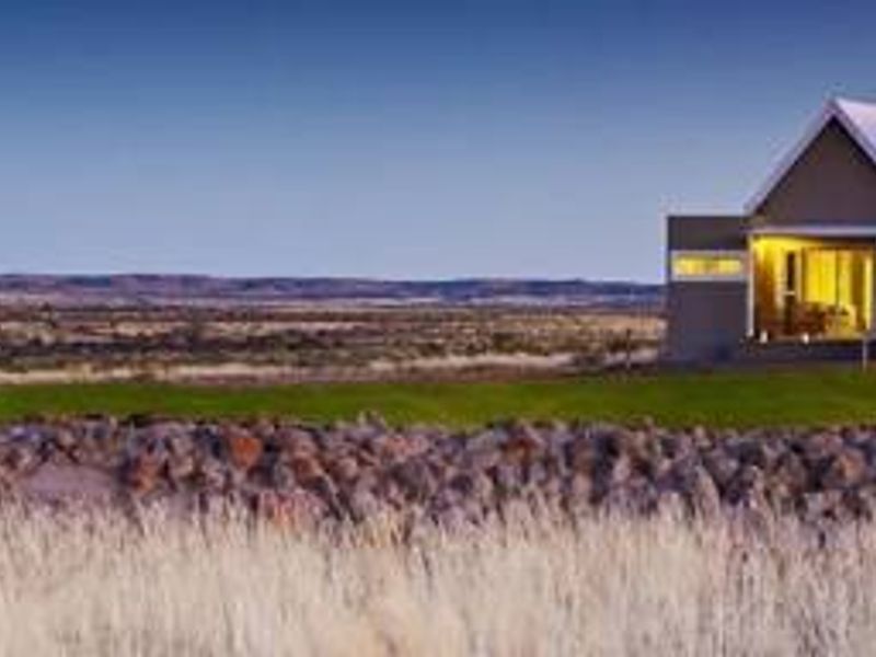 A modern farmhouse with dual pitched roofs and expansive glass doors, set against a vast rural landscape with a traditional stone wall in the foreground.
