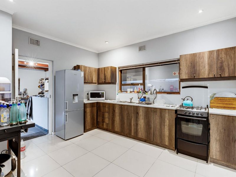 A functional kitchen featuring wood-look cabinetry, laminate countertops, tiled flooring, and a freestanding gas stove with an integrated oven.
