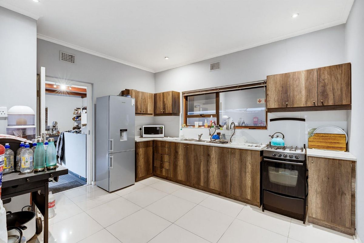 A functional kitchen featuring wood-look cabinetry, laminate countertops, tiled flooring, and a freestanding gas stove with an integrated oven.