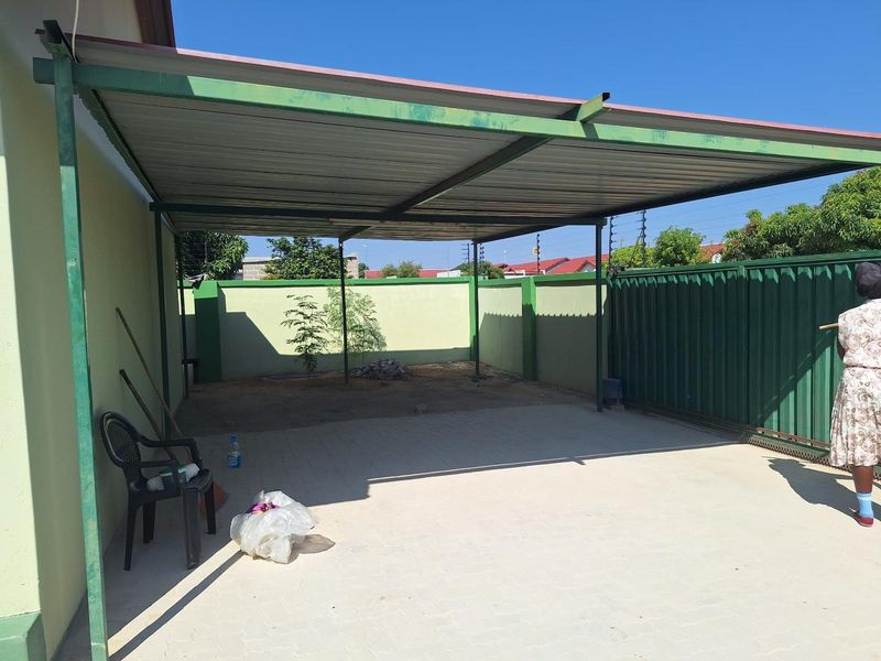 A covered outdoor carport area featuring paved flooring, a metal roof structure, and secure perimeter walling with electric fencing.