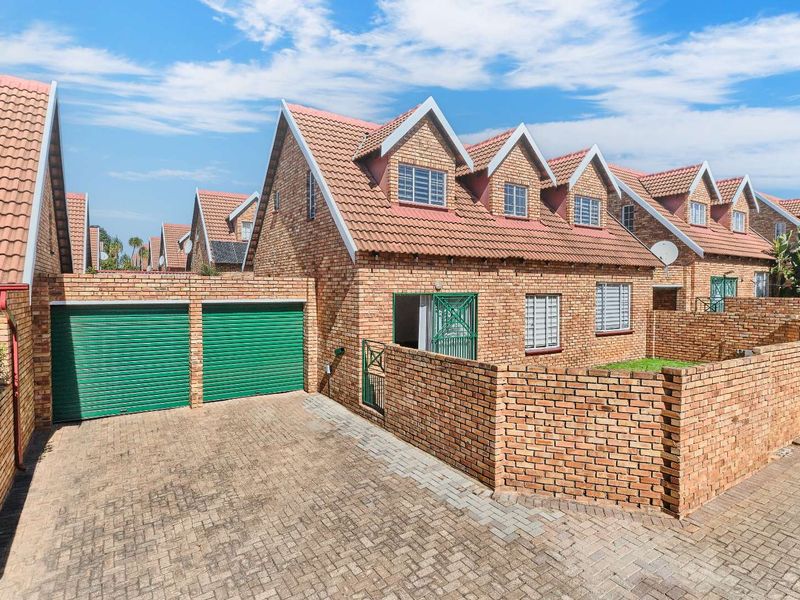 Front view of a face-brick townhouse featuring a double garage, paved driveway, and a private enclosed garden area.