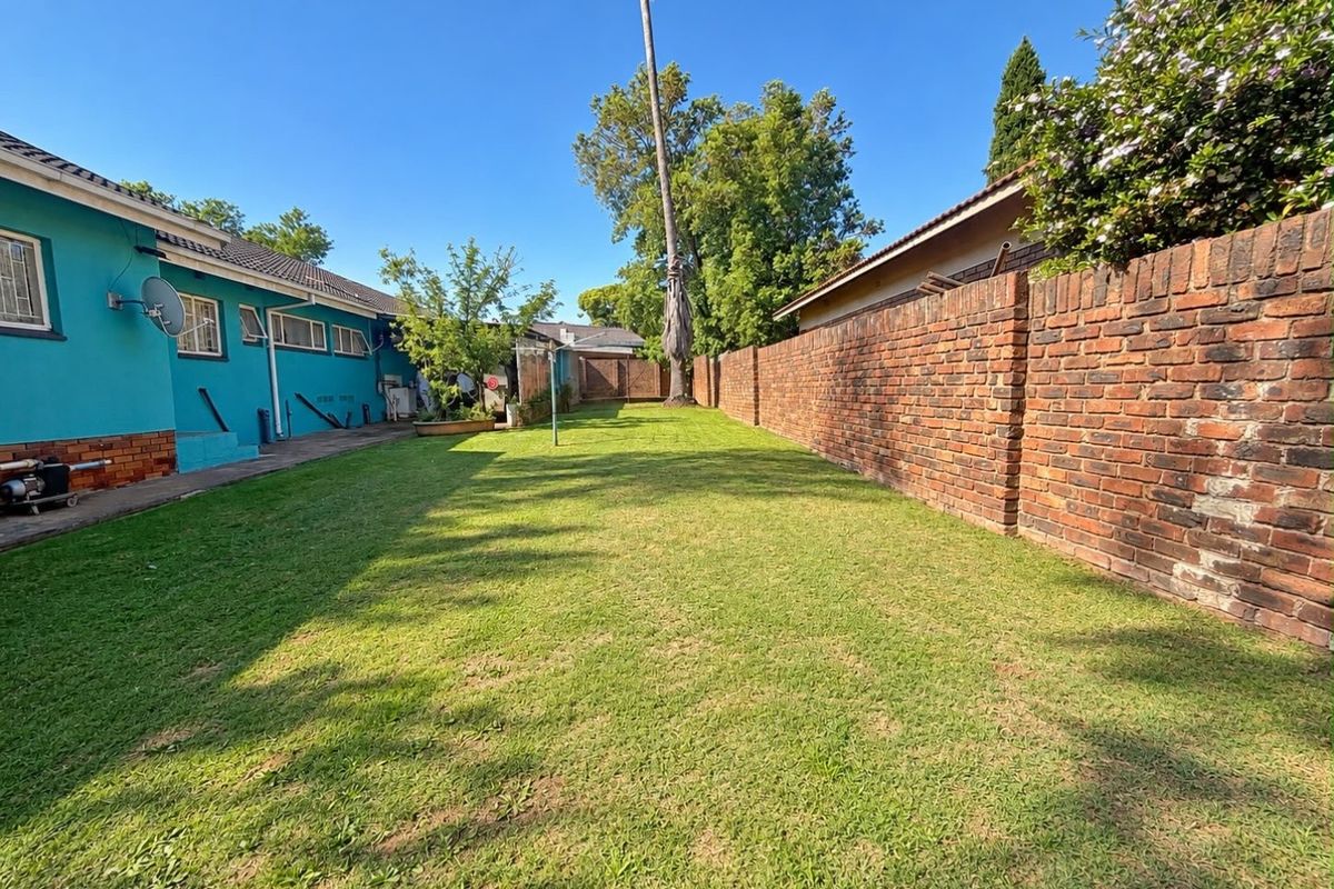 A spacious rear garden featuring a well-maintained lawn, a long brick boundary wall, and a concrete pathway along the side of the house.