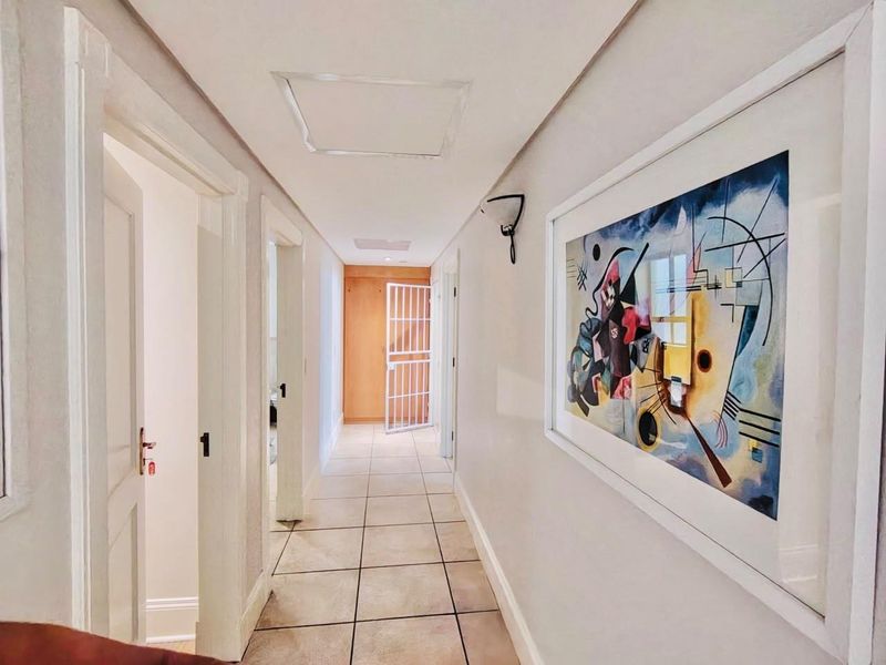 A clean, well-lit hallway featuring neutral tiled flooring and multiple doorways leading to adjacent rooms, with a security gate visible at the far end.