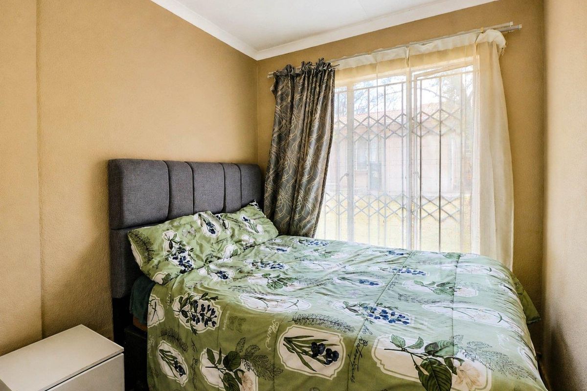 A cozy bedroom featuring neutral wall tones, a window with a fitted security gate, and classic coving detail.